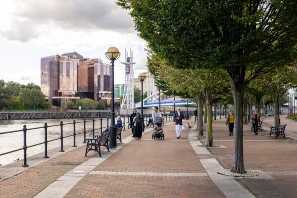 A group of people walking on a sidewalk by a body of water