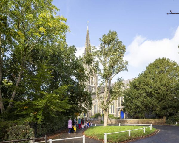 A group of people walking in front of a church surrounded by trees